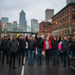A diverse group of NAACP supporters and protestors stand united with raised fists at a peaceful demonstration in Portland.